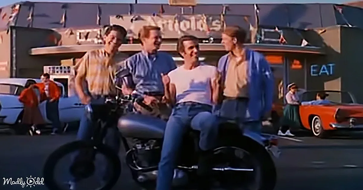 Four young men on a motorcycle in front of Arnold's diner, smiling and enjoying the moment.