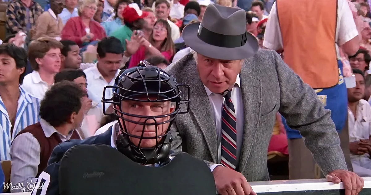 A man in a gray suit leans over a catcher in a baseball game, surrounded by spectators.