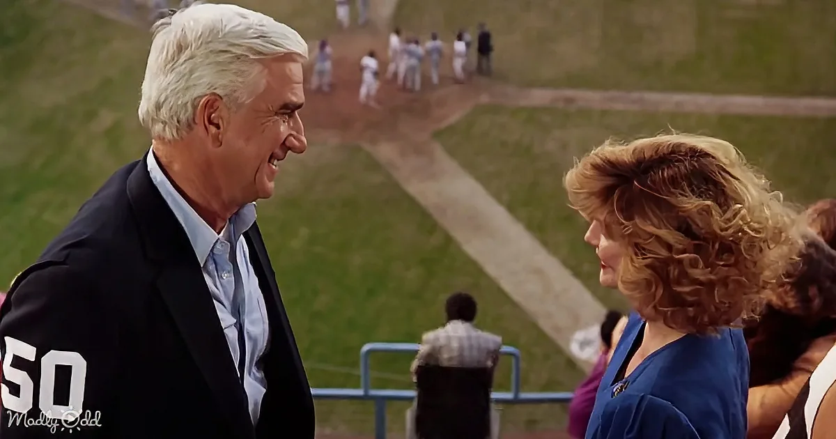 A man in a suit with "50" on his back is smiling at a woman in a blue dress at a sports field.
