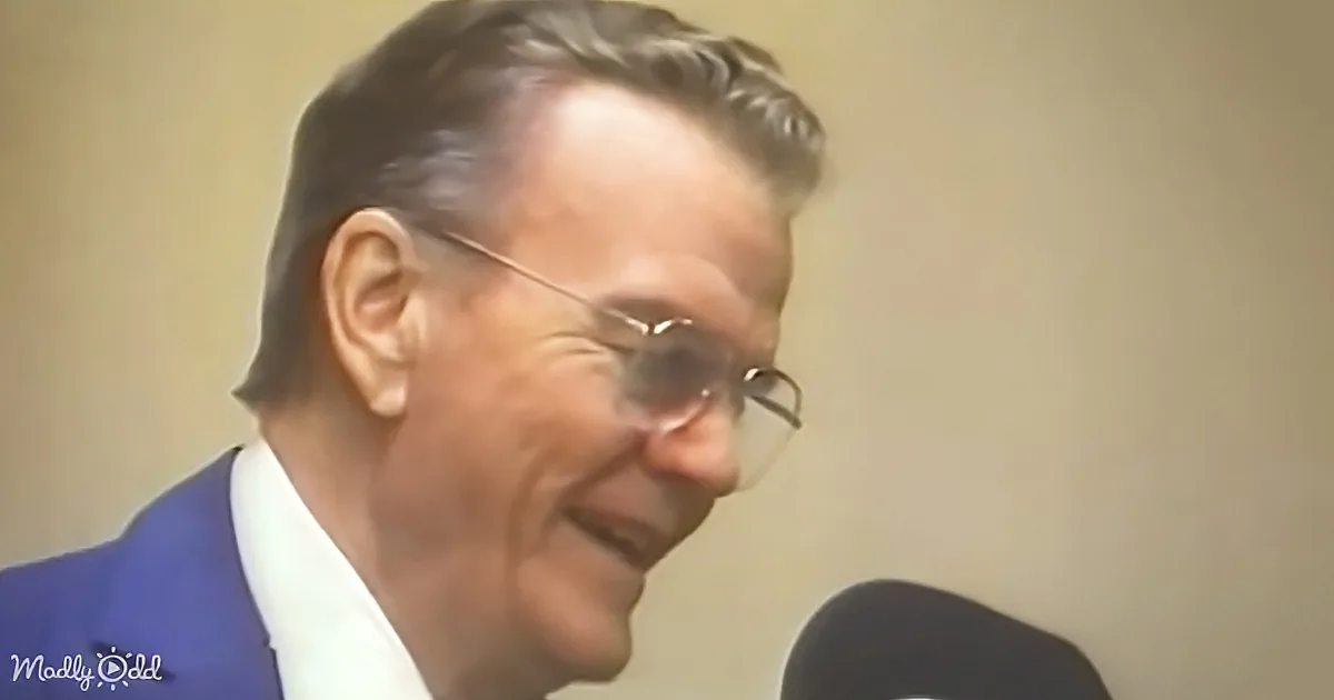 A man in a blue suit and glasses is smiling near a microphone.