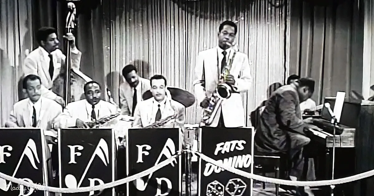 A jazz band performs with Fats Domino's name prominently displayed on their instruments.