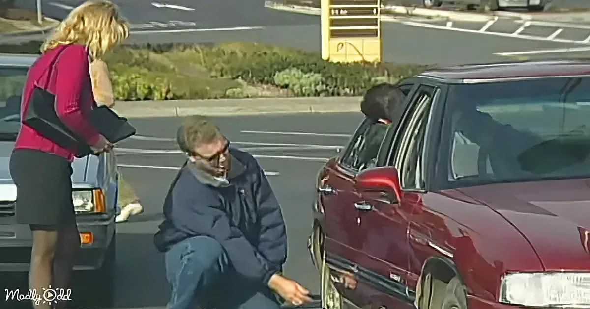 A man kneels in a parking lot, holding a ring, while a woman stands nearby, looking at him.