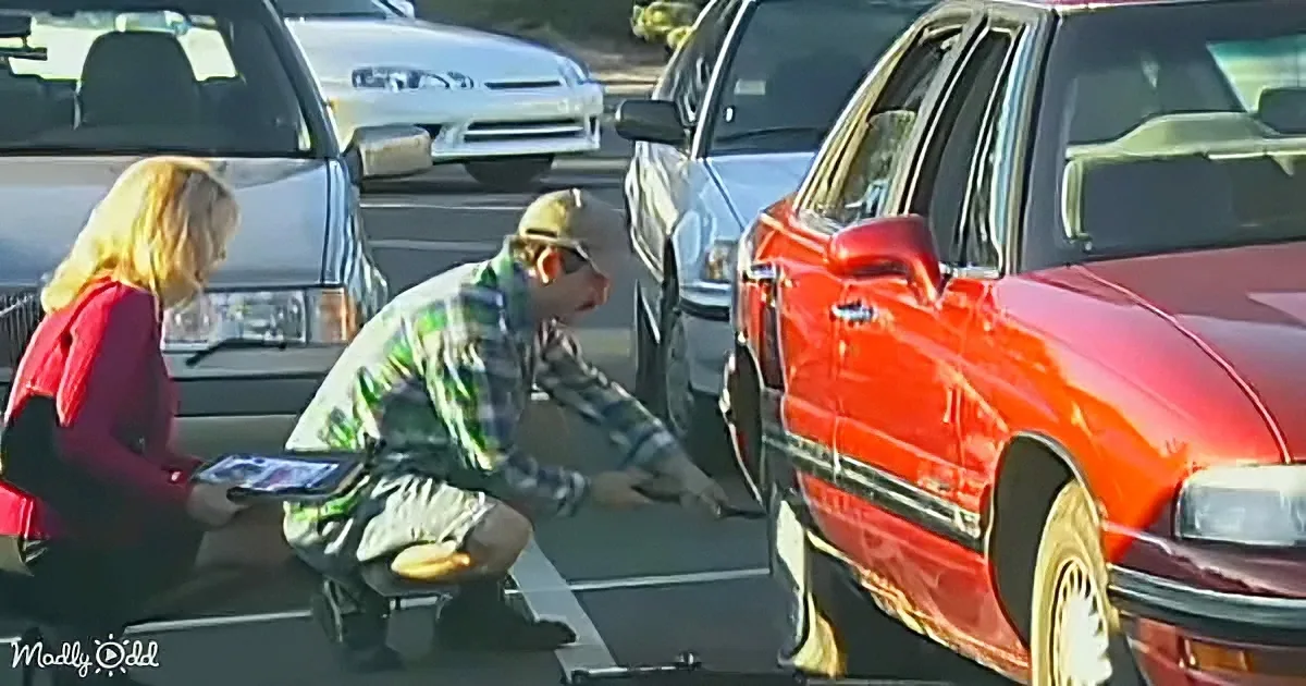 A man in a plaid shirt and hat is kneeling beside a red car, seemingly inspecting it, while a woman in a red jacket...