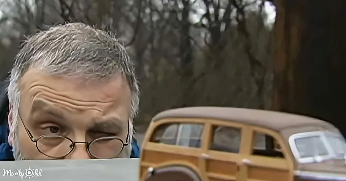 A man with glasses closely examines a model of a wooden station wagon.