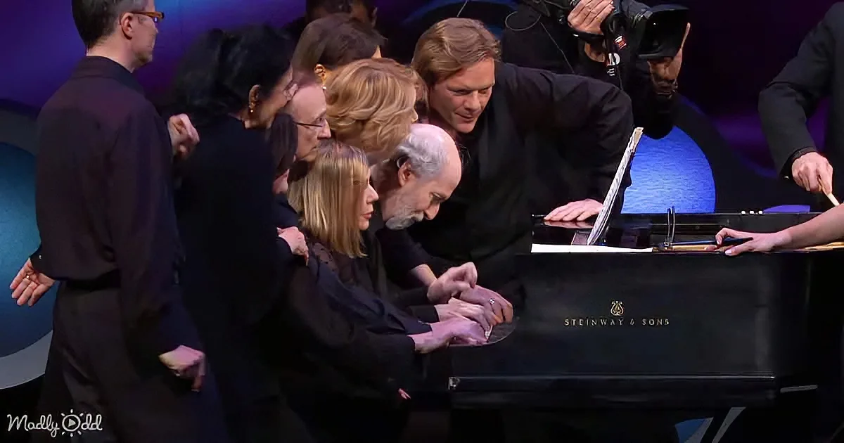 A man plays a Steinway & Sons grand piano surrounded by a group of people.