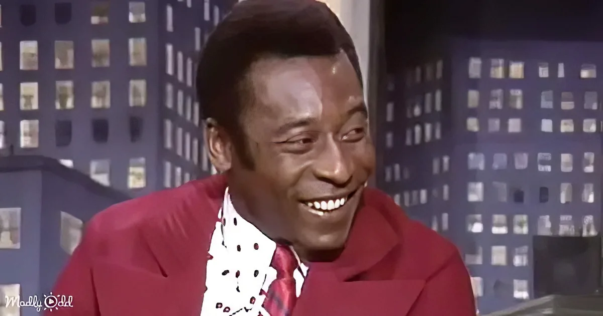 A man in a red suit and white shirt with black polka dots is smiling.