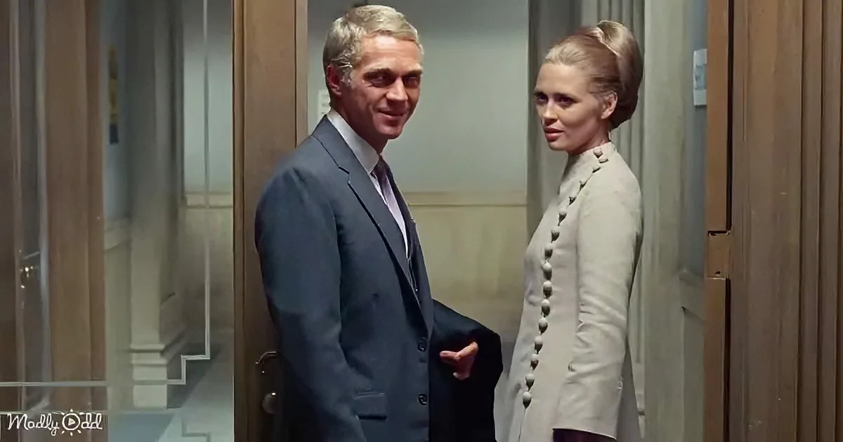 A man in a suit and a woman in a dress stand in an elevator, both looking at the camera.