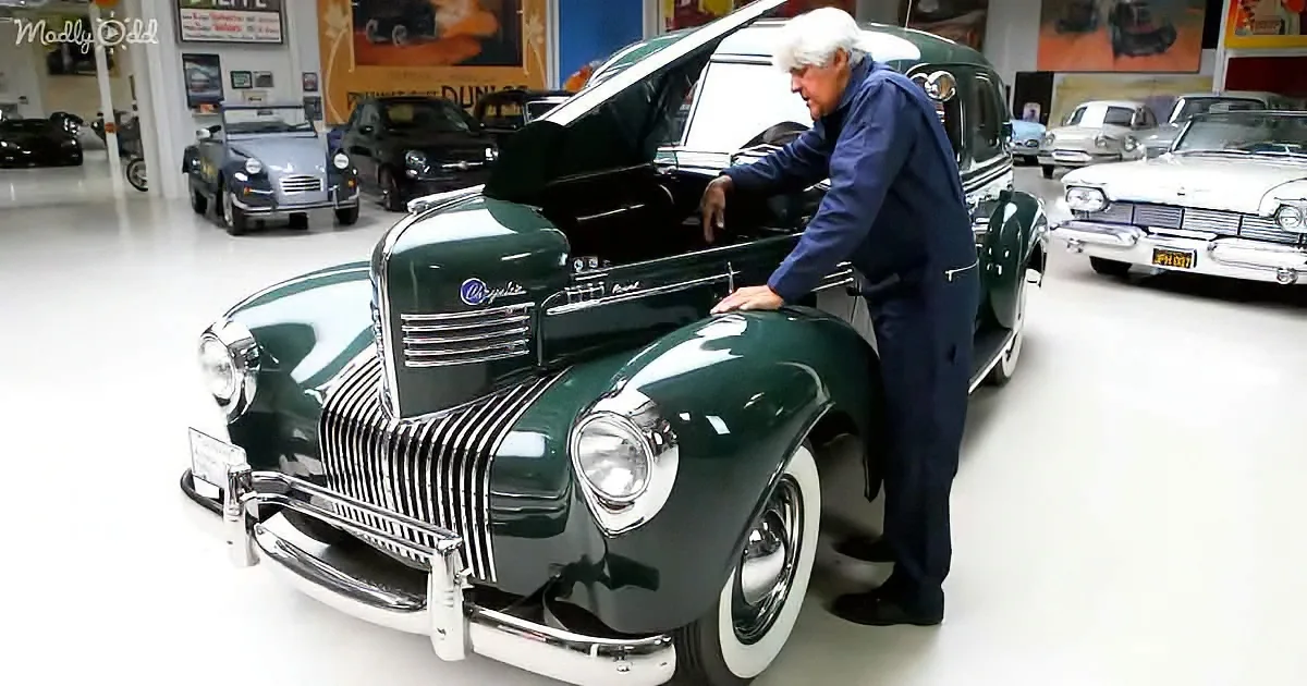 A man in a blue suit examines a classic green car in a showroom filled with vintage vehicles.