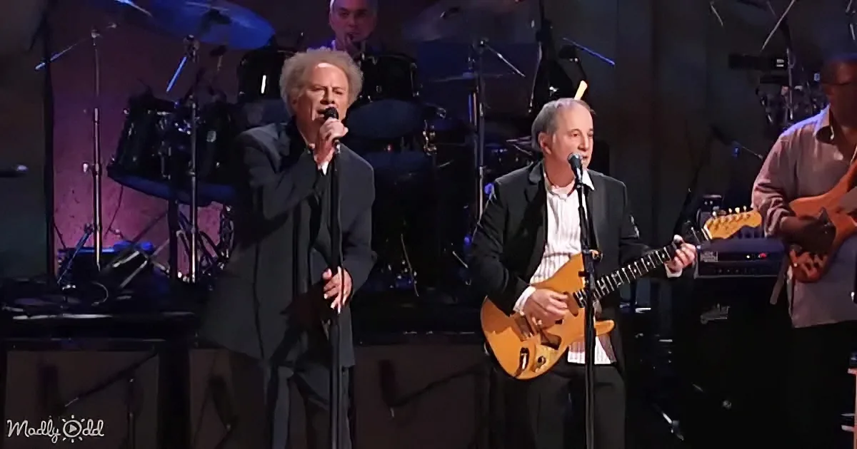 A man in a suit sings into a microphone while another plays guitar on stage.