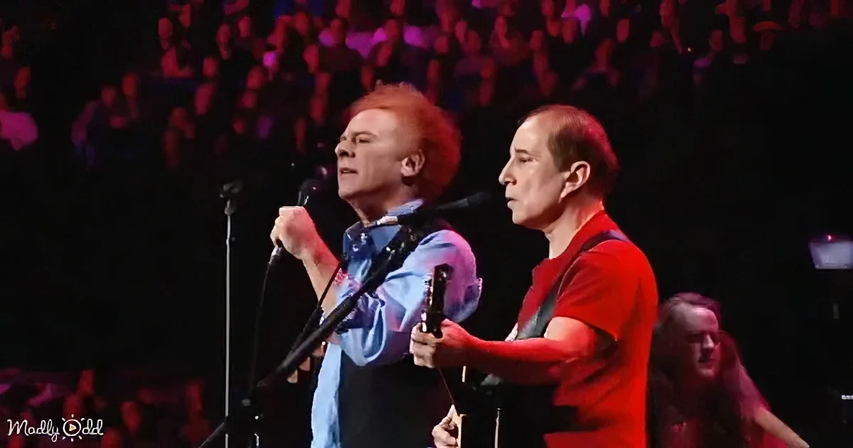 Two musicians perform on stage, one singing into a microphone, the other playing guitar.