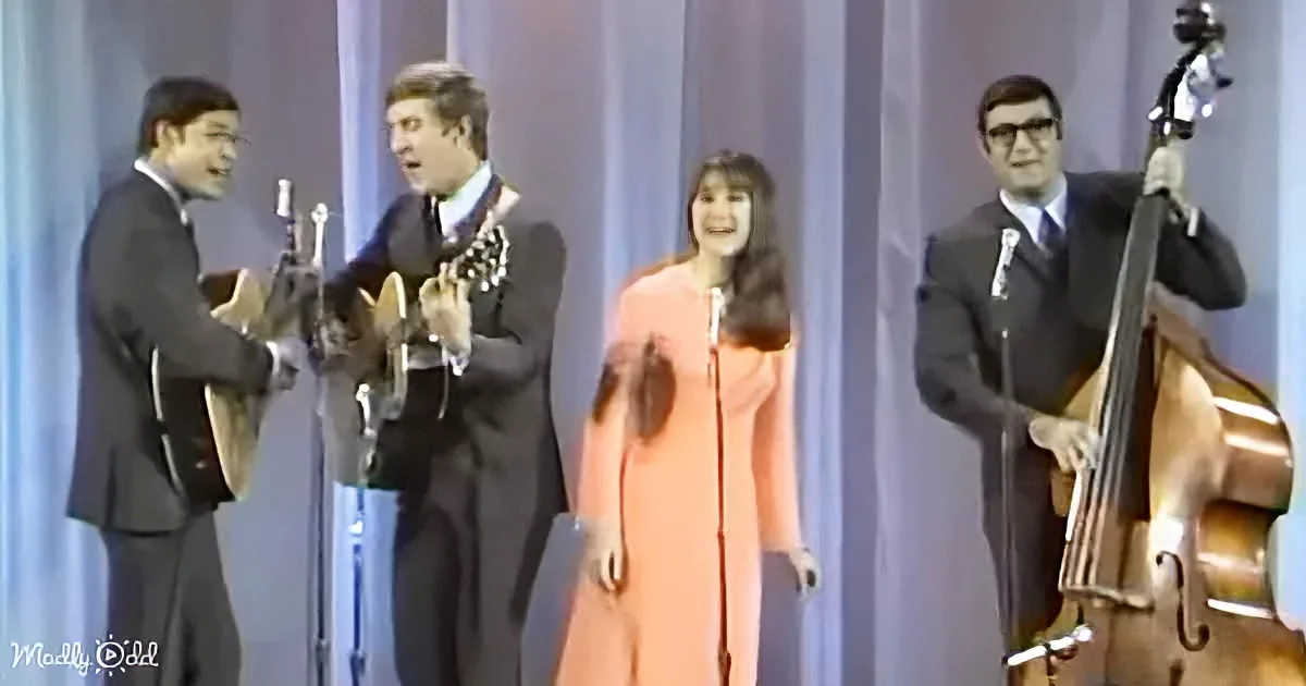 A woman in an orange dress sings on stage with a band playing instruments.