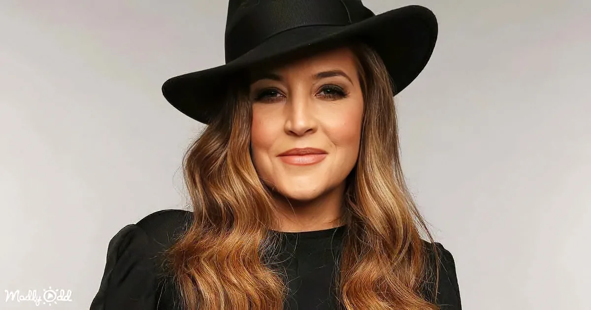 A woman with long, wavy hair and a black hat smiles against a plain background.
