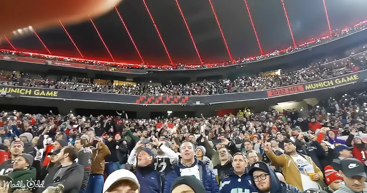 A large crowd of excited fans in a stadium, cheering and raising their hands, with "MUNICH GAME" and "2022 NFL" signage...