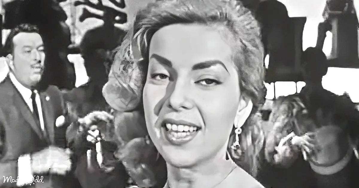 A smiling woman with styled hair and earrings, surrounded by people in a social setting.