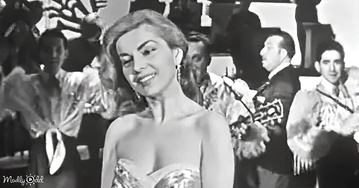 A woman in a strapless dress smiles amidst a lively band and audience in a black-and-white scene.