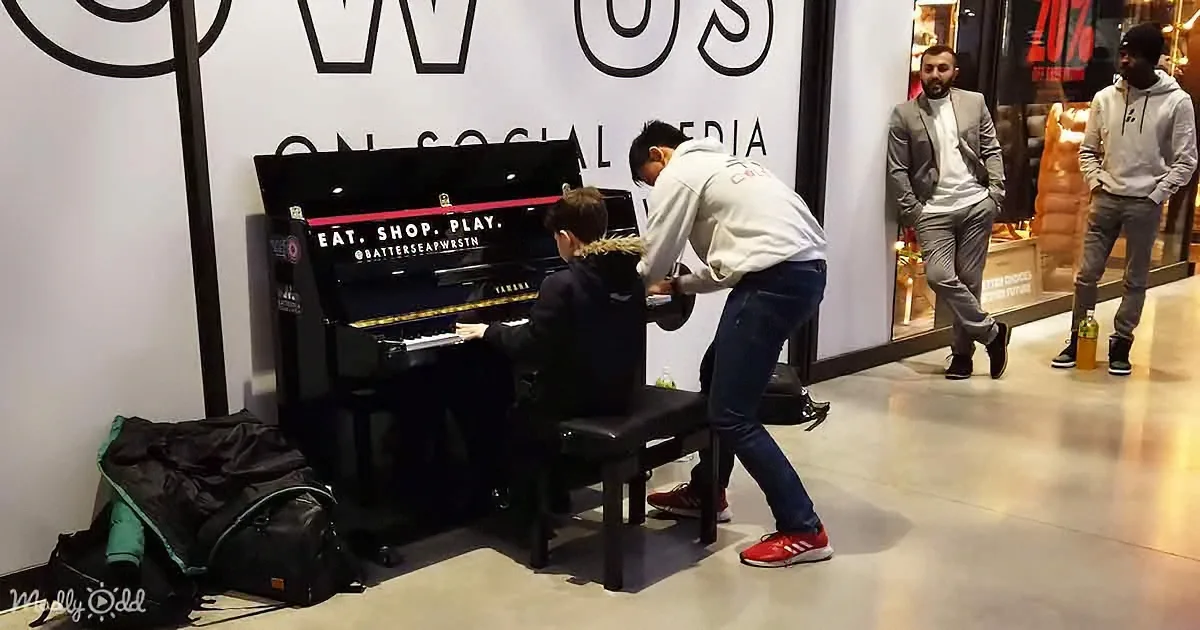 A child plays piano while an adult assists, in a shopping mall setting.