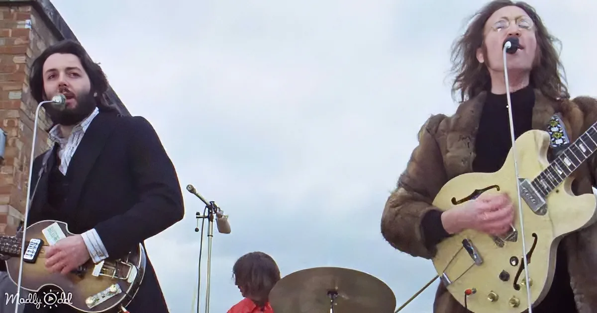 A man in a fur coat plays guitar while another man in a suit sings into a microphone.