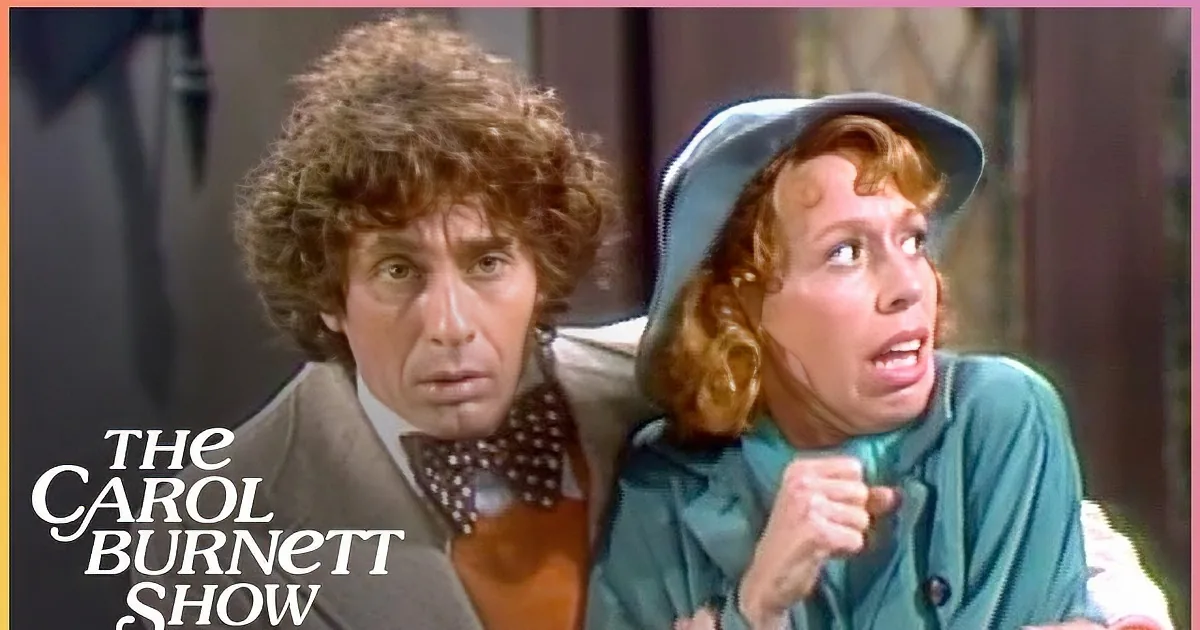 A man in a beige suit and bow tie stands behind a woman in a teal outfit and hat, both appearing surprised.