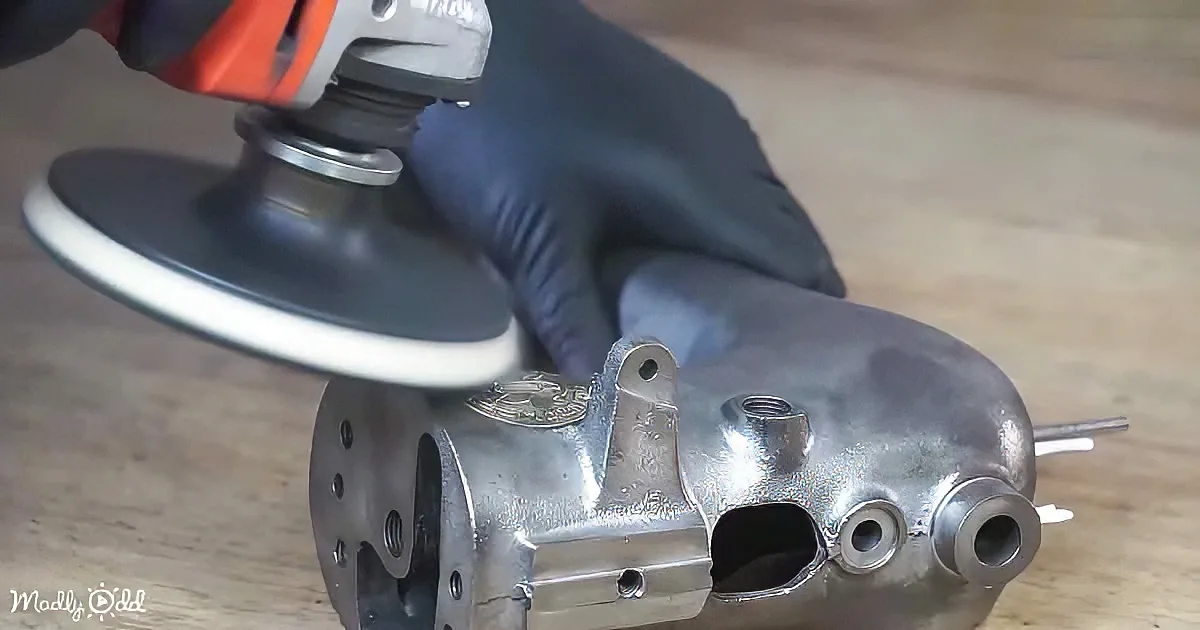 A gloved hand uses a sander on a metallic engine part.