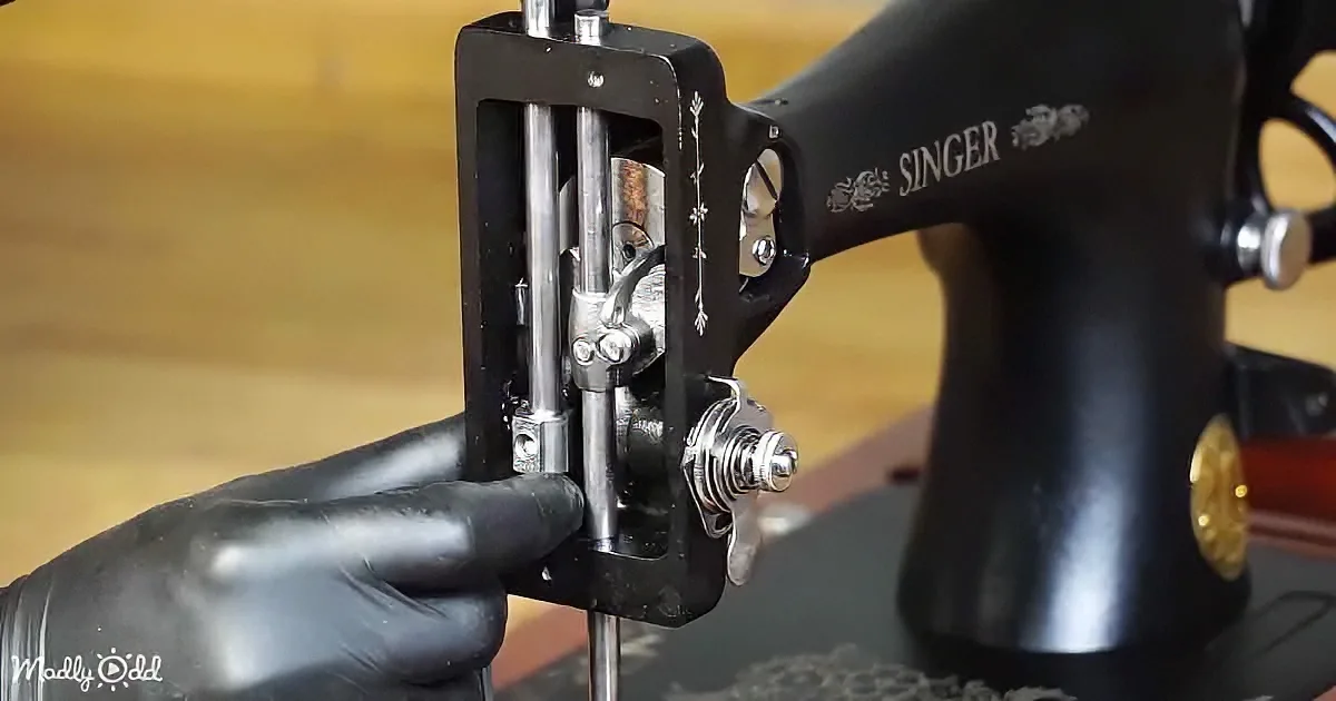 A hand in a black glove adjusts the presser foot on a Singer sewing machine.