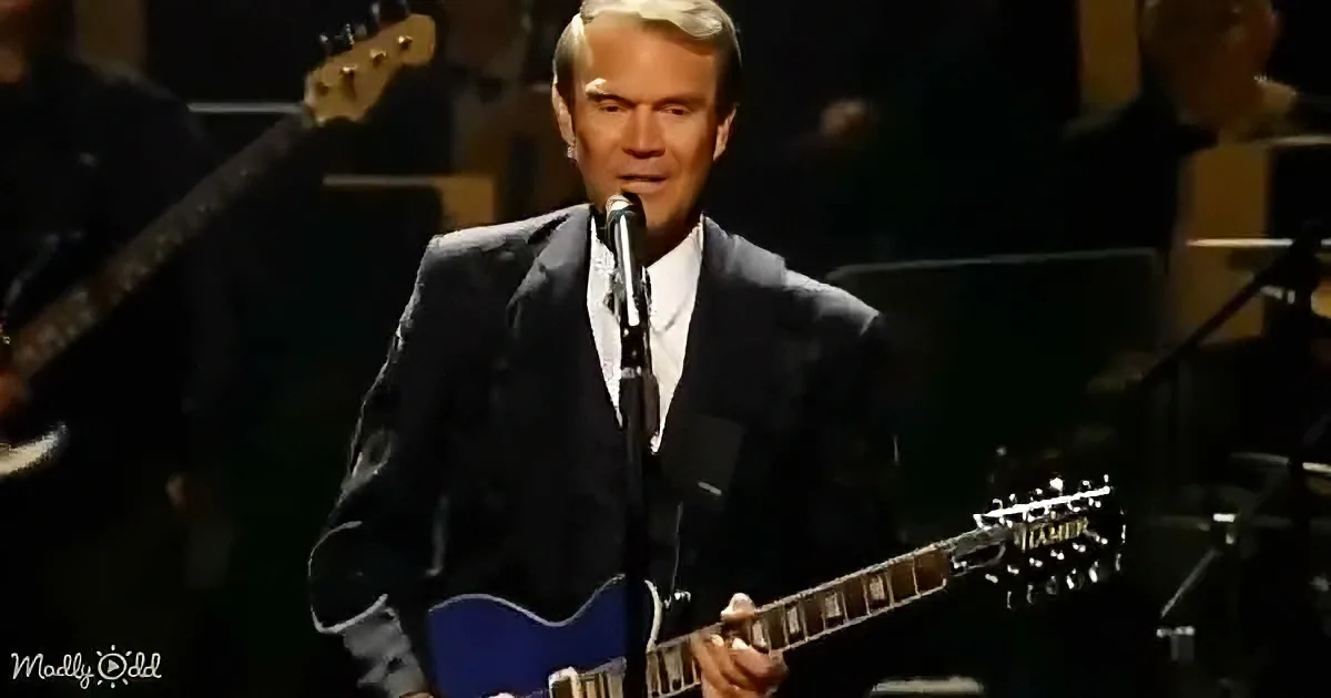 A man in a suit plays a blue guitar on stage, singing into a microphone.