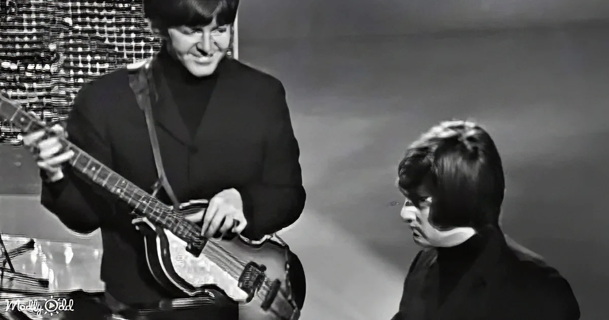 A man in a suit plays a bass guitar while another man in a suit looks on.