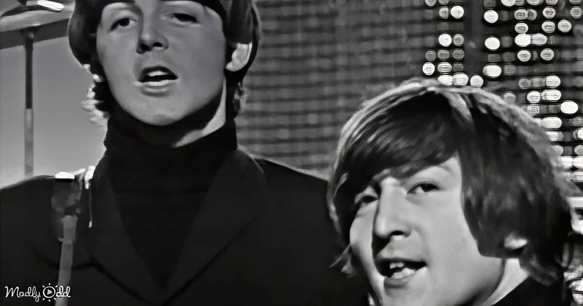 A man in a turtleneck sings into a microphone, with another person partially visible behind him.