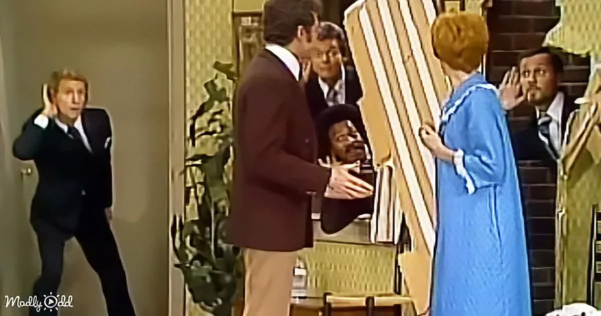 A man in a suit is being held by another man in a maroon suit, while a woman in a blue dress stands nearby, and a man in...