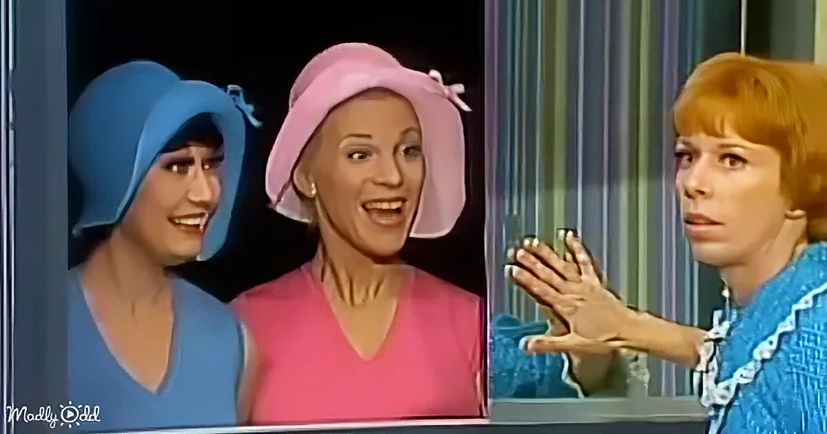 Two women in colorful outfits, one in blue, the other in pink, are smiling and interacting with a third woman in a blue...