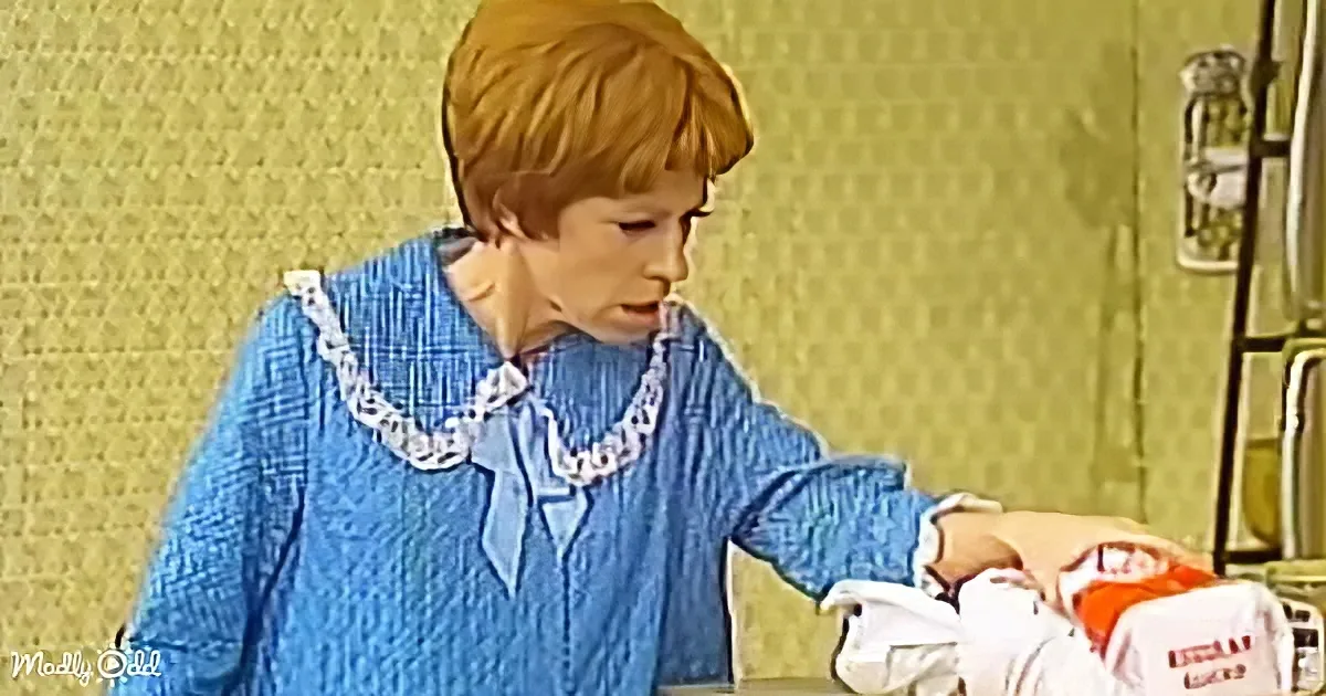 A woman in a blue dress with a white lace collar is reaching for something on a counter.