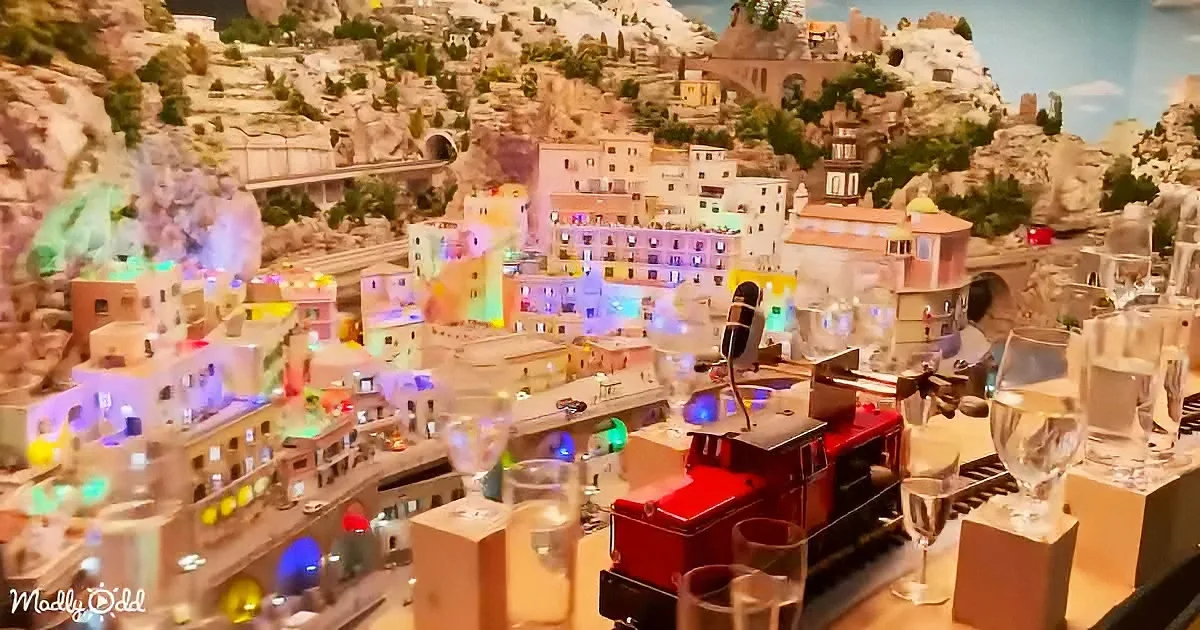 A miniature model of a colorful town with a red train and glass barriers.