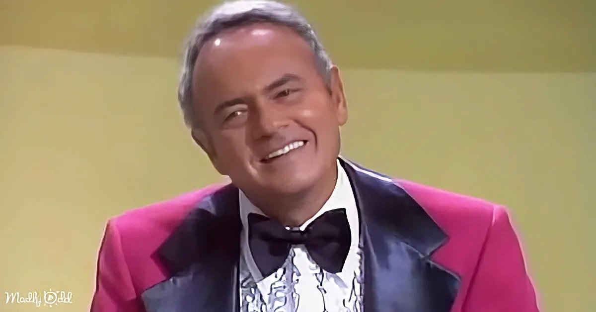 A man in a vibrant pink suit with a black bow tie smiles warmly.
