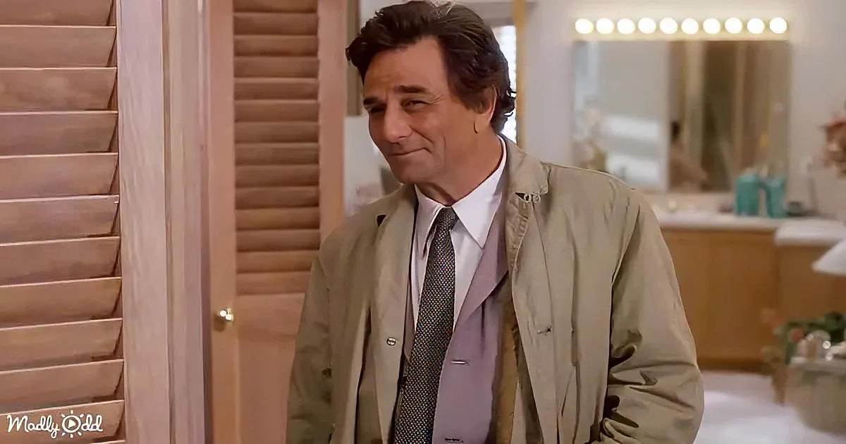 A man in a beige jacket and tie stands in a room with wooden shutters and a mirror with lights.