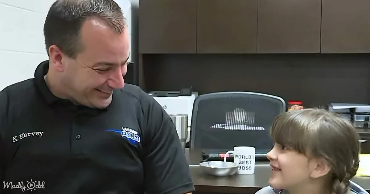 A man in a police uniform smiles at a young girl in a kitchen setting.
