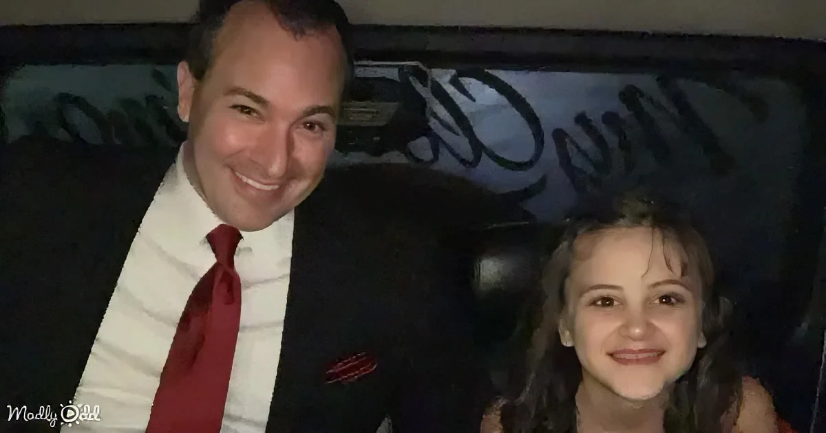 A man in a suit and red tie sits next to a young girl with dark hair, both smiling.