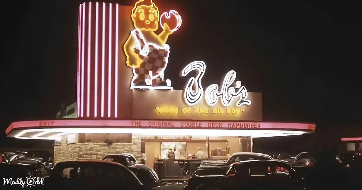 A neon sign featuring a cartoon boy holding a hamburger adorns the Bob's Big Boy restaurant at night.