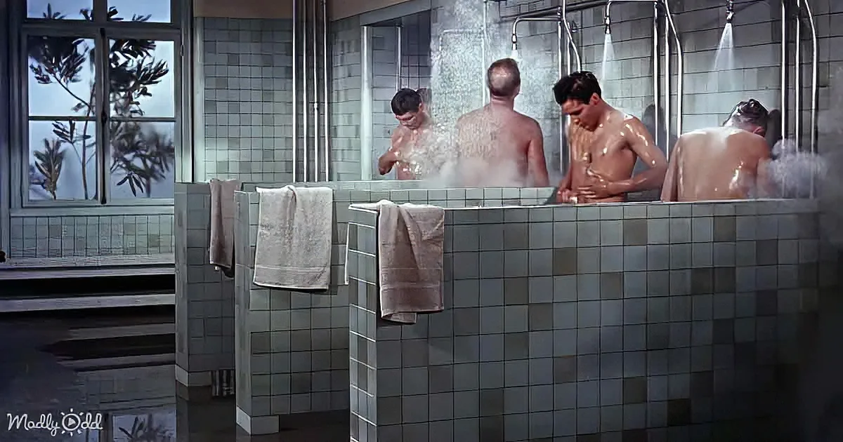 Four men are in a steamy, tiled shower area with water spraying over them.