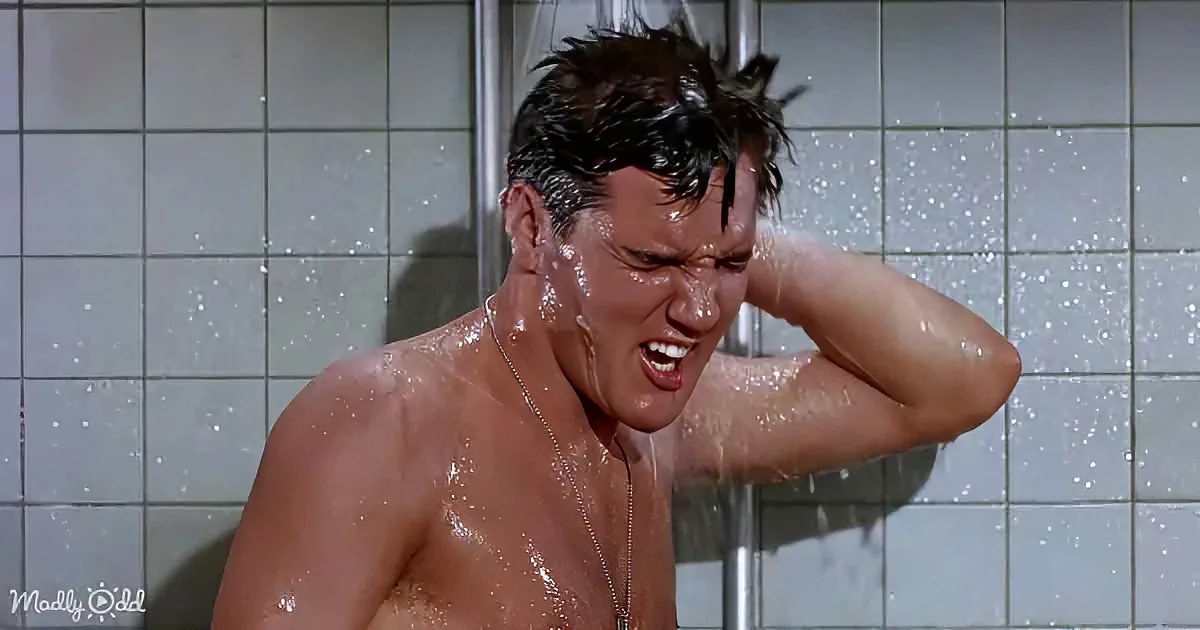 A man with wet hair and shirtless is in a shower, holding his head in distress.