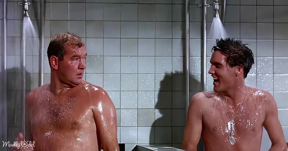 Two men in a shower, one laughing, both wet, with water splashing around them.