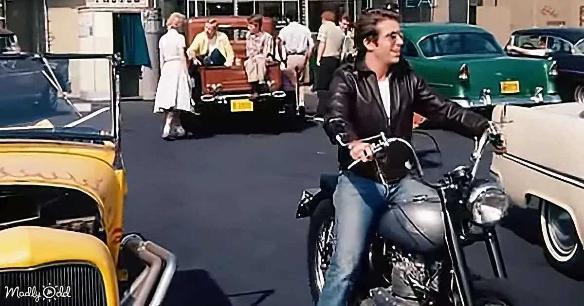 A man in a leather jacket rides a motorcycle in a bustling street scene with vintage cars and people.