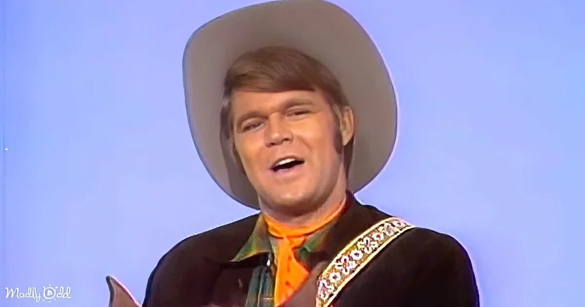 A man in a cowboy hat and western attire is singing, with a bright orange scarf and a blue background.