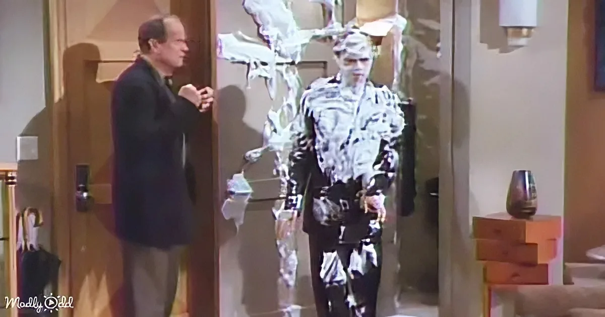 A person in a white and black costume stands in a doorway, while another person in a suit observes.