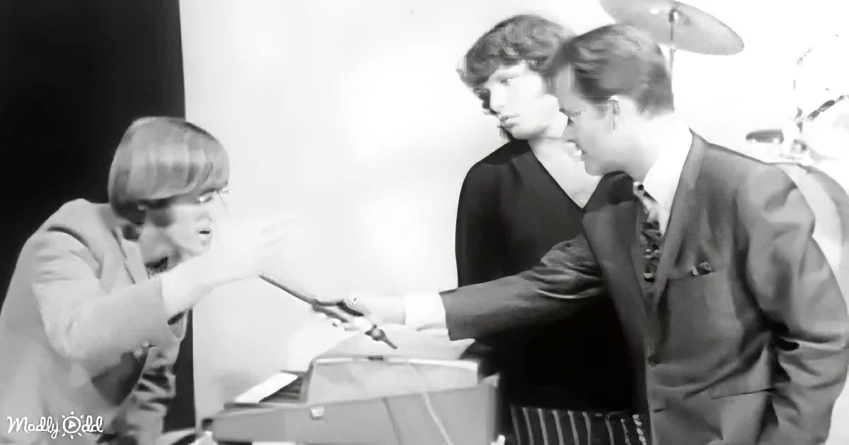 A man in a suit holds a pen, interacting with another man in a white shirt, while a third man in a dark shirt observes in...