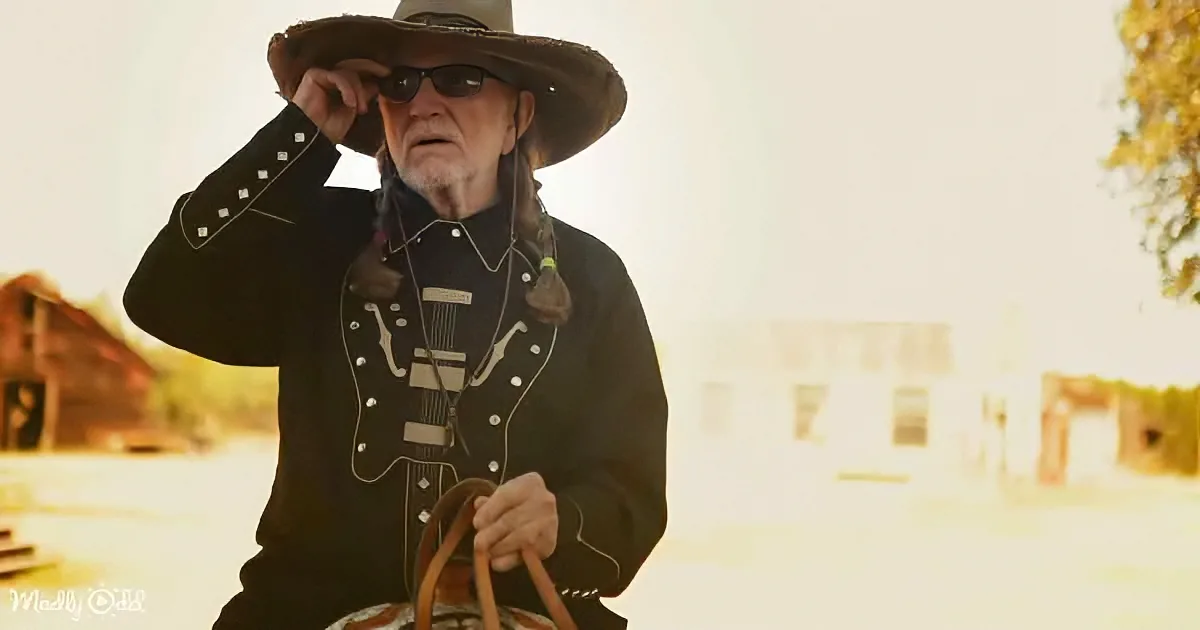 A man in a cowboy hat and black outfit holds a basket, standing in a sunlit, rustic setting.