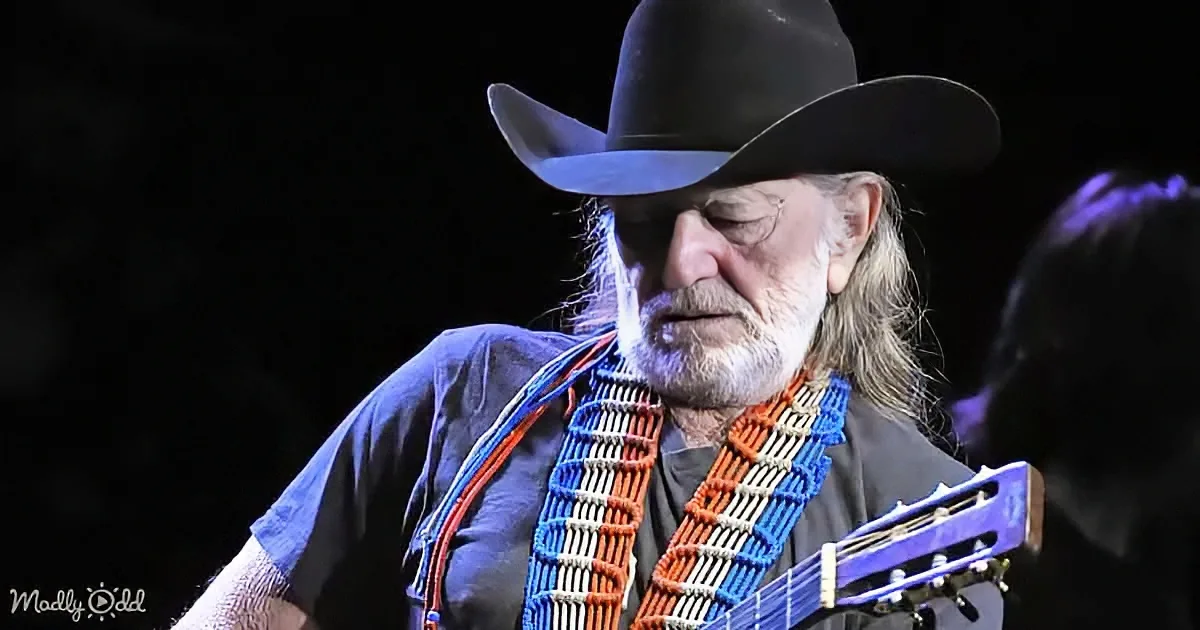 A man in a cowboy hat and blue shirt plays a guitar with a colorful strap.