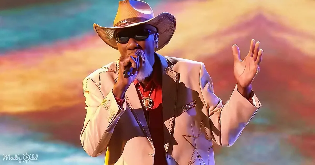 A man in a cowboy hat and sunglasses performs passionately on stage, holding a microphone.