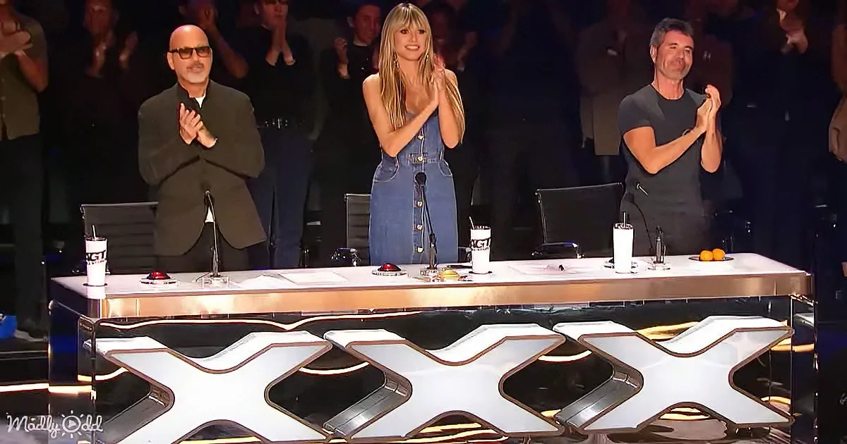 Three judges clapping at a table with a large "X" design, audience in the background.