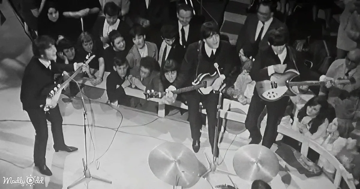 The Beatles perform on stage with guitars and microphones, surrounded by an audience.