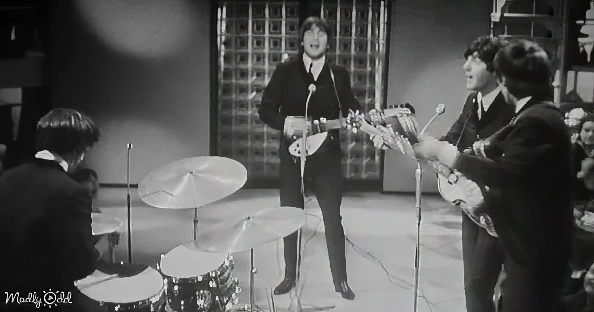The Beatles perform on stage, John Lennon sings, Paul McCartney plays bass, Ringo Starr drums, George Harrison plays guitar.