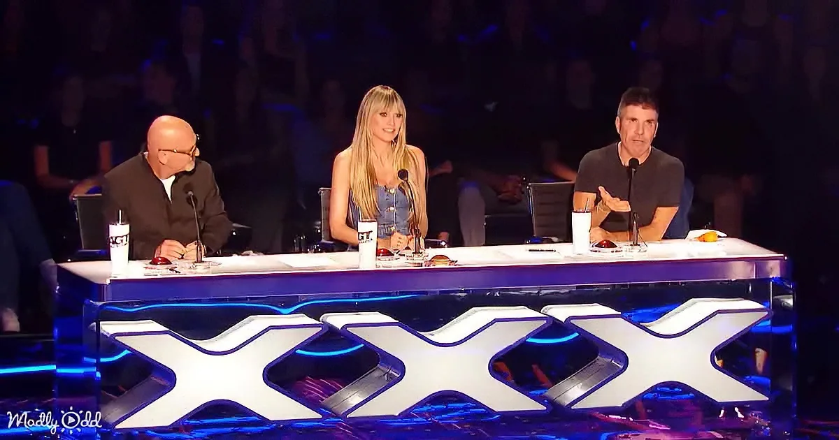 Three judges sit at a table with a large "XXX" logo, likely from a talent show, with a dark audience in the background.